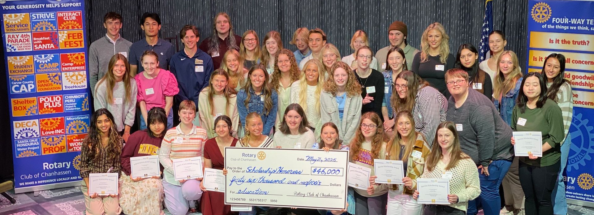 Group of people holding certificates, large check, posing for photo. Banner behind them.