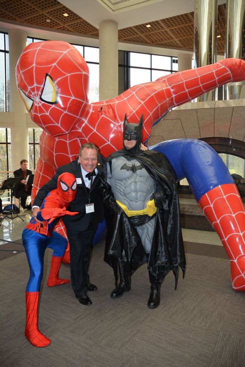 Man in suit with Batman and two Spider-Man figures inside building; large inflatable Spider-Man in background.