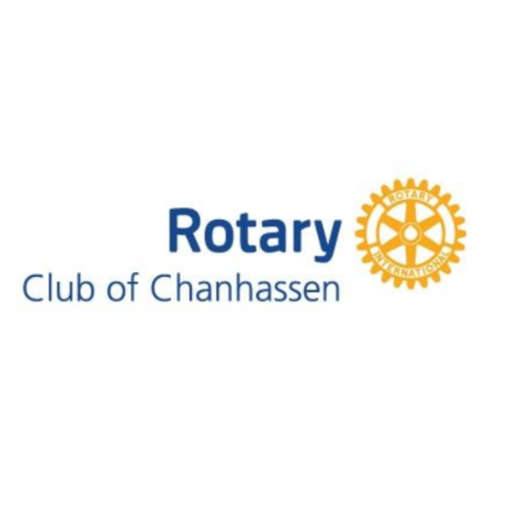 Rotary Club meeting; people seated at tables, speaker at podium showing a slide, American flag in background.