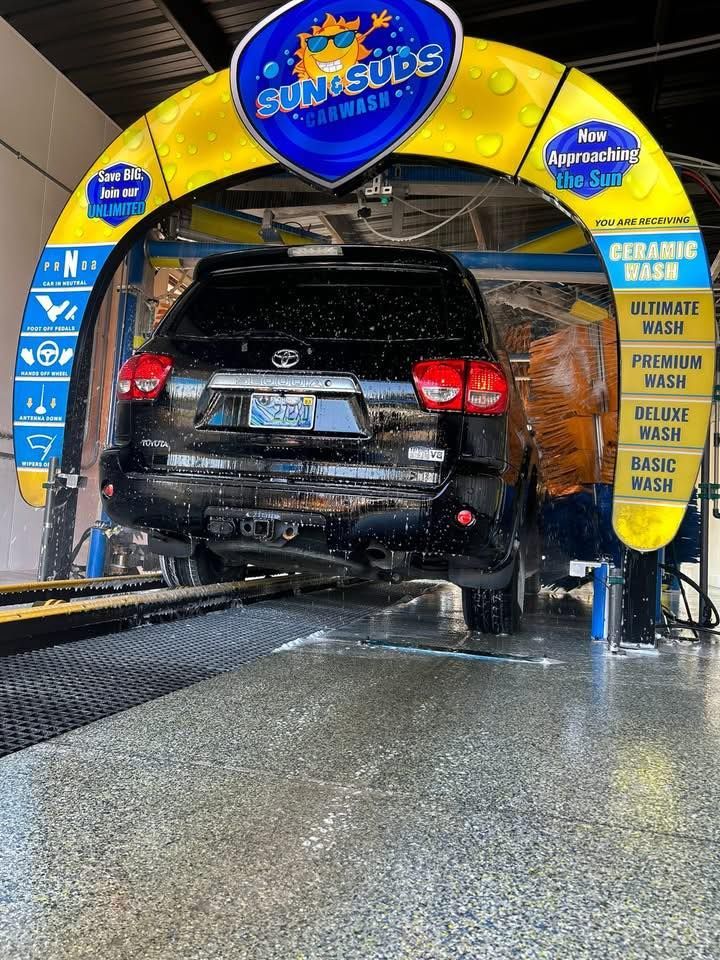 Black SUV in a yellow car wash tunnel being sprayed with water.