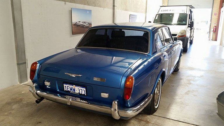 A blue car is parked in a garage next to a white van.