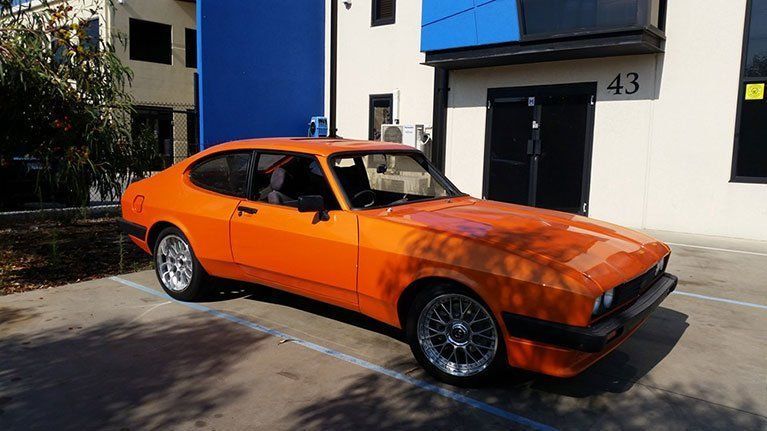 An orange car is parked in a parking lot in front of a building.