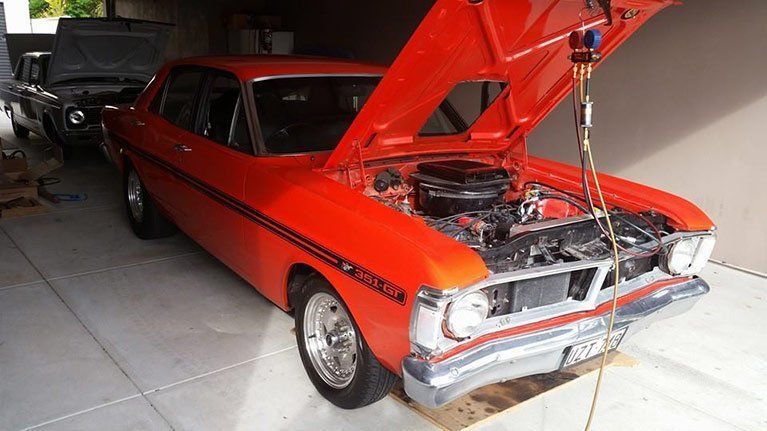 An orange car with the hood up in a garage