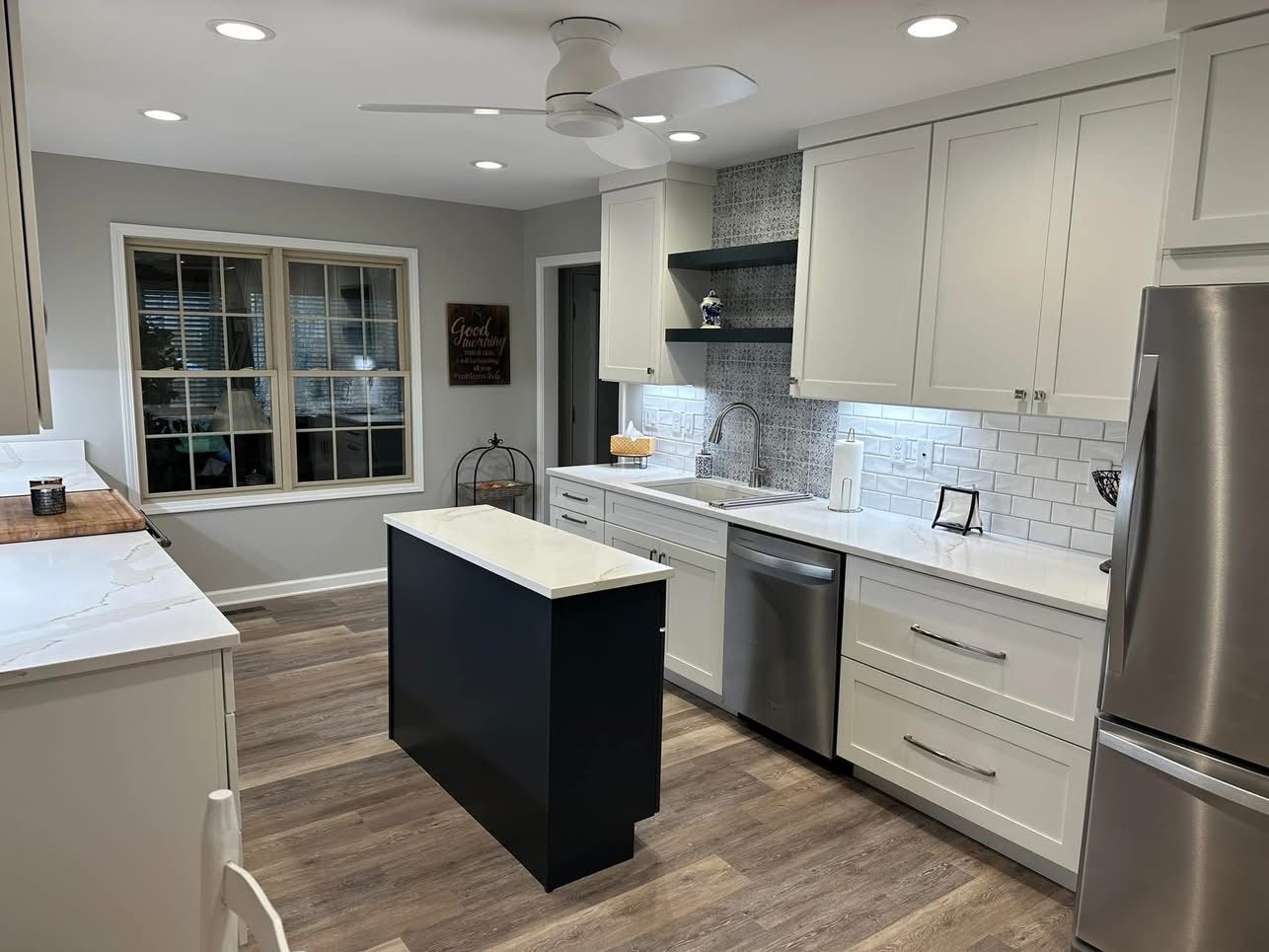 A kitchen with white cabinets , stainless steel appliances , a large island and a ceiling fan.