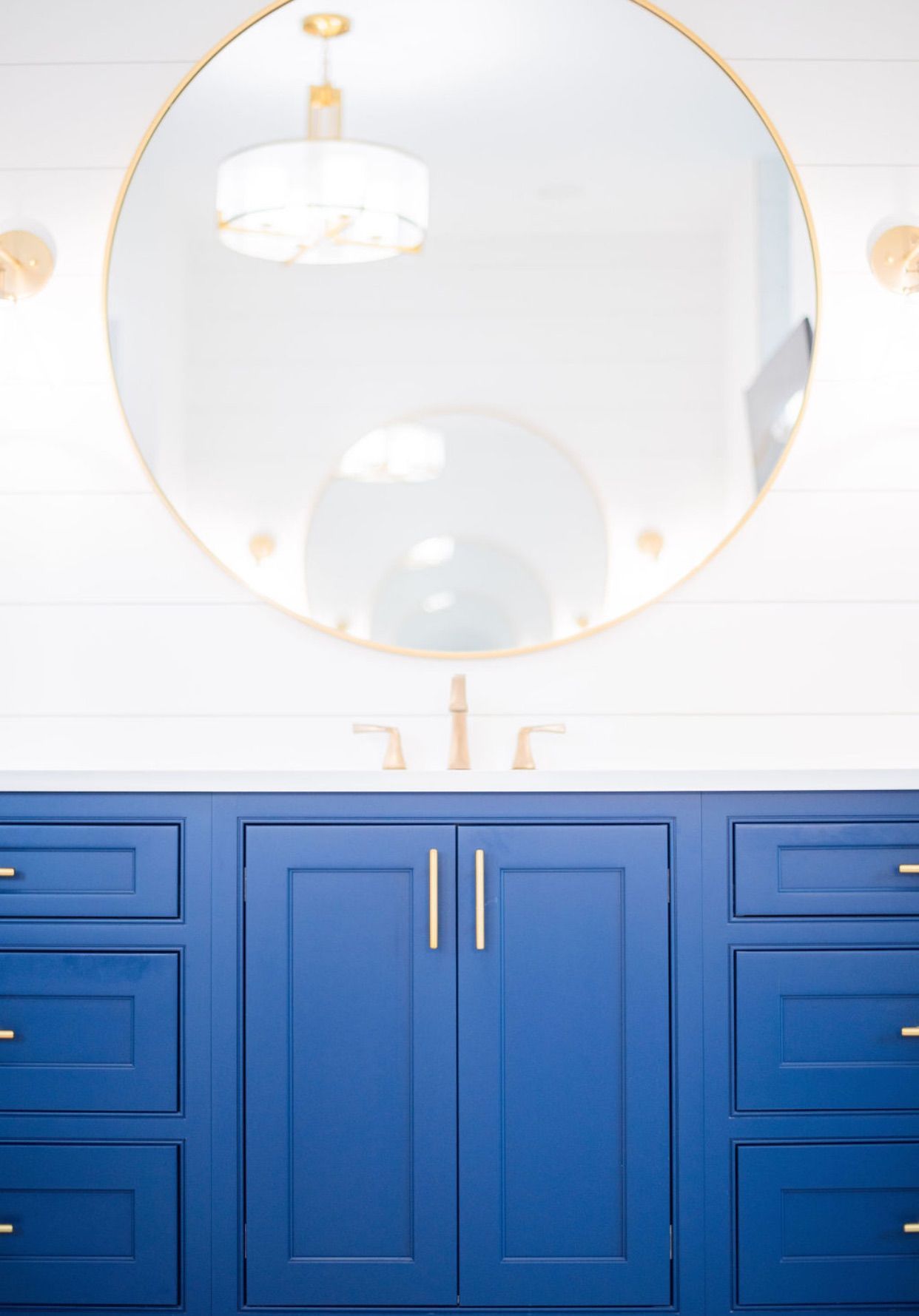 A bathroom vanity with blue cabinets and a round mirror.