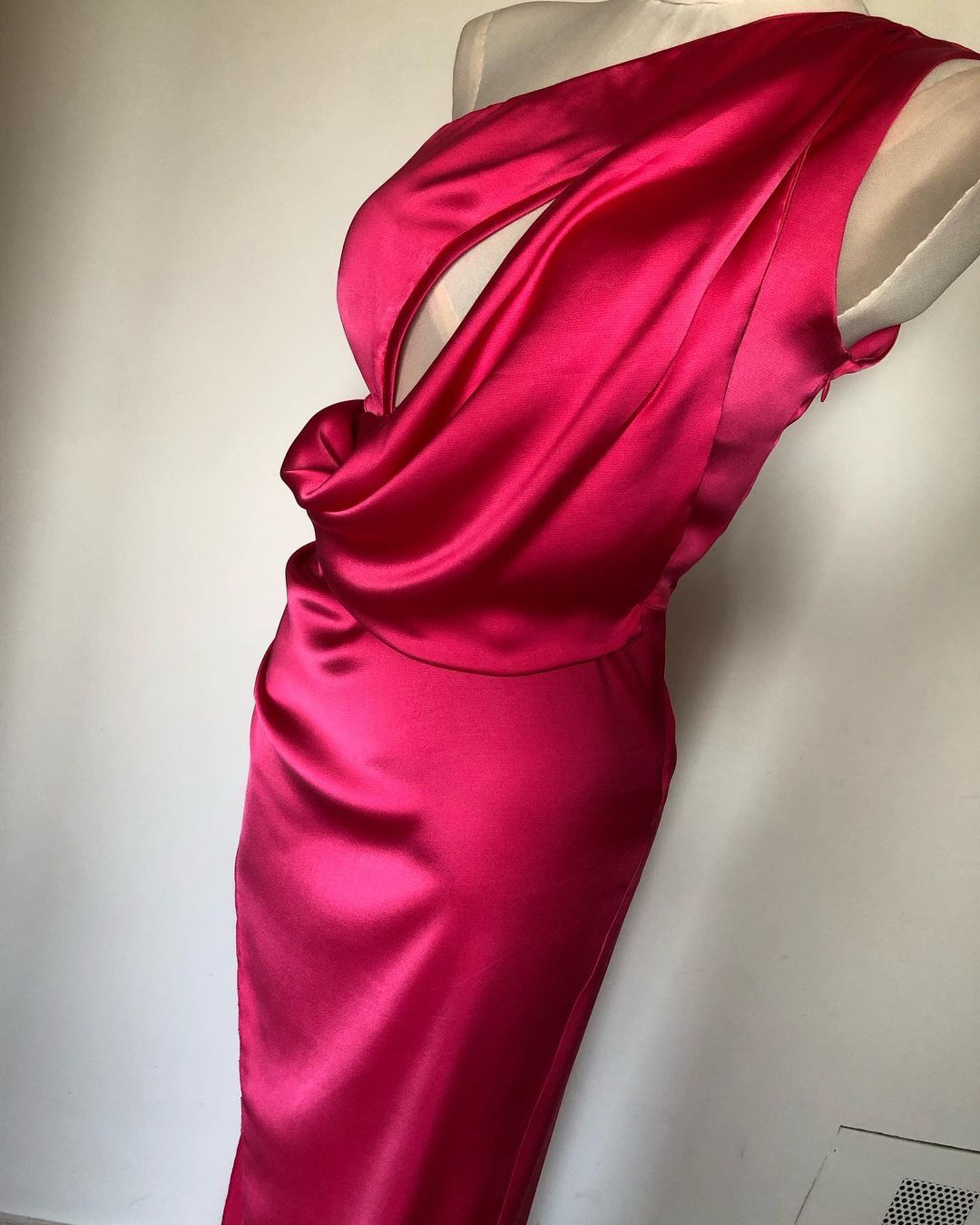 Un vestido rosa está sobre un maniquí contra una pared blanca.