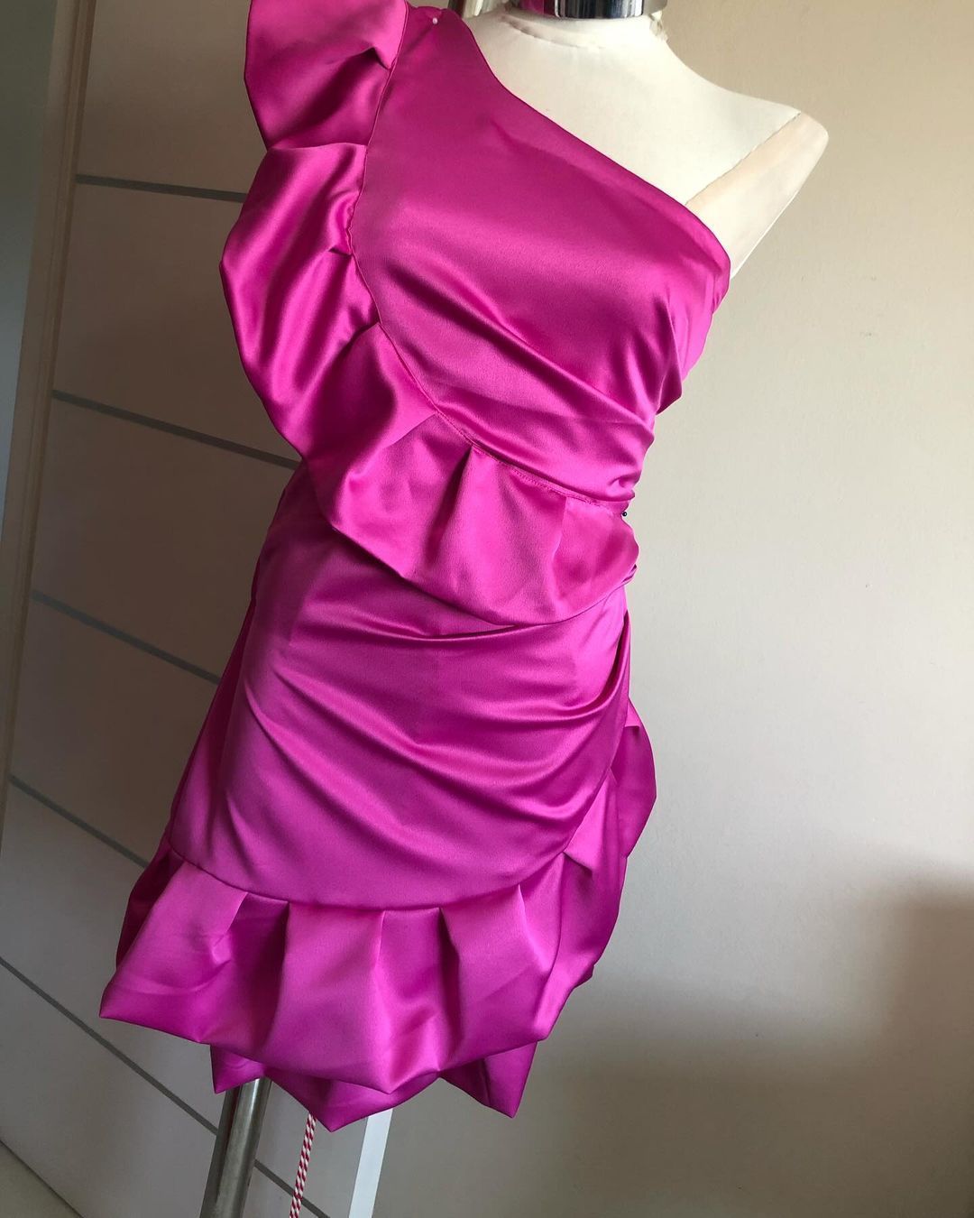 Un vestido rosa de un solo hombro con volantes está sobre un maniquí.