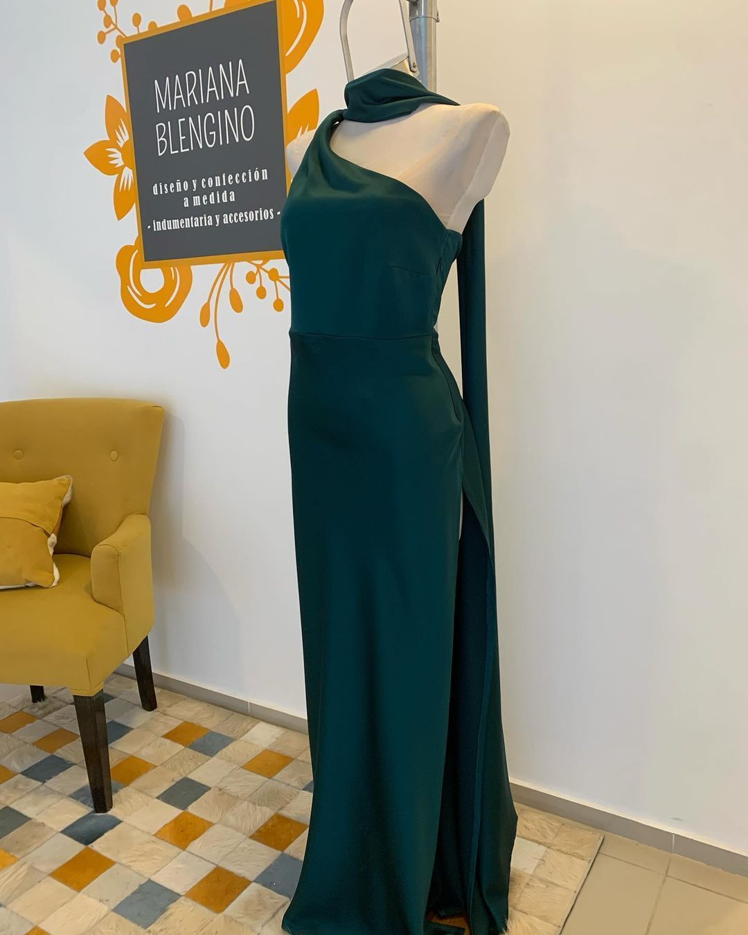 Un vestido verde está sobre un maniquí frente a un cartel que dice Mariana Fleng MD