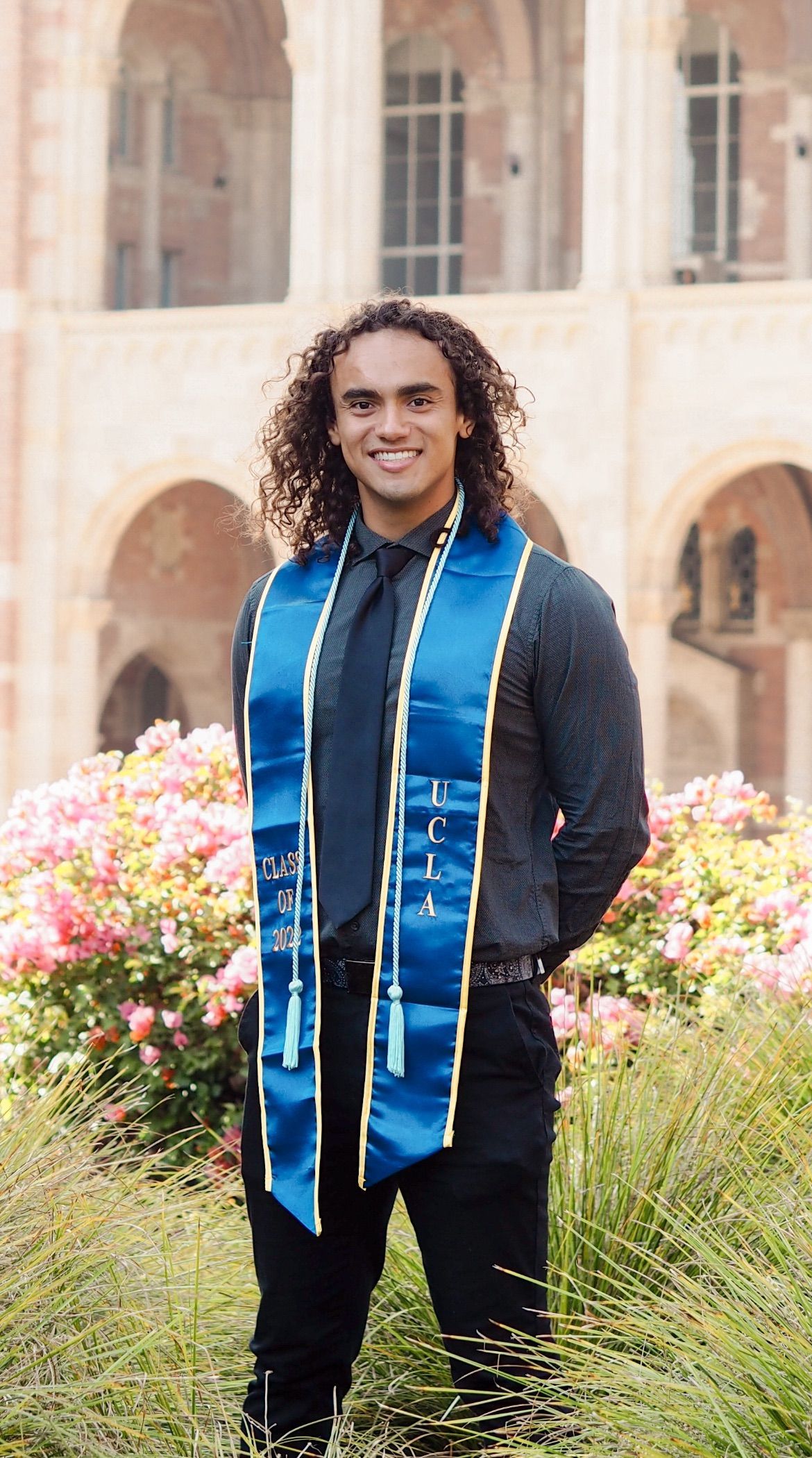A man wearing a blue sash and tie is standing in front of a building.
