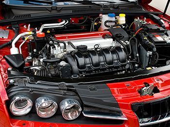 the engine of a red car is visible under the hood .