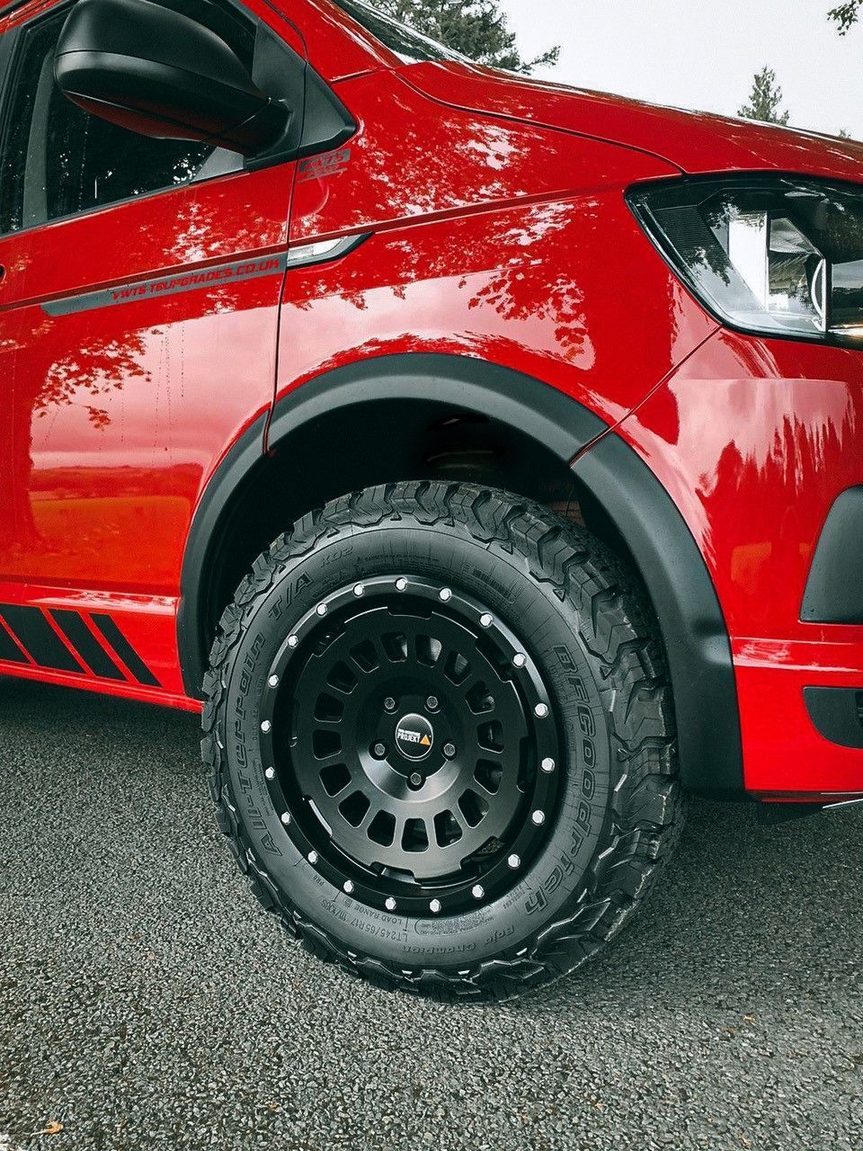Rode bestelwagen met zwarte offroad-velgen en spatbordverbreders op een asfaltweg.