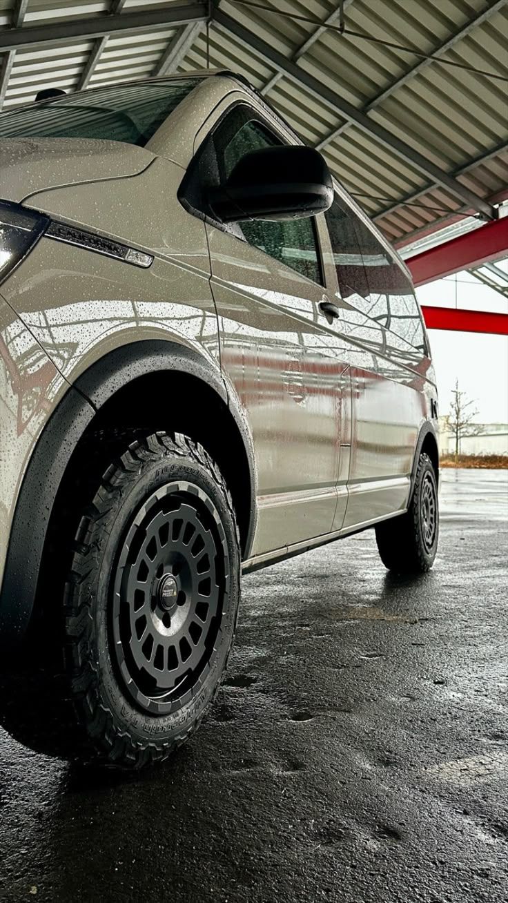 Witte bestelwagen met zwarte banden geparkeerd onder een afdak op een natte ondergrond.