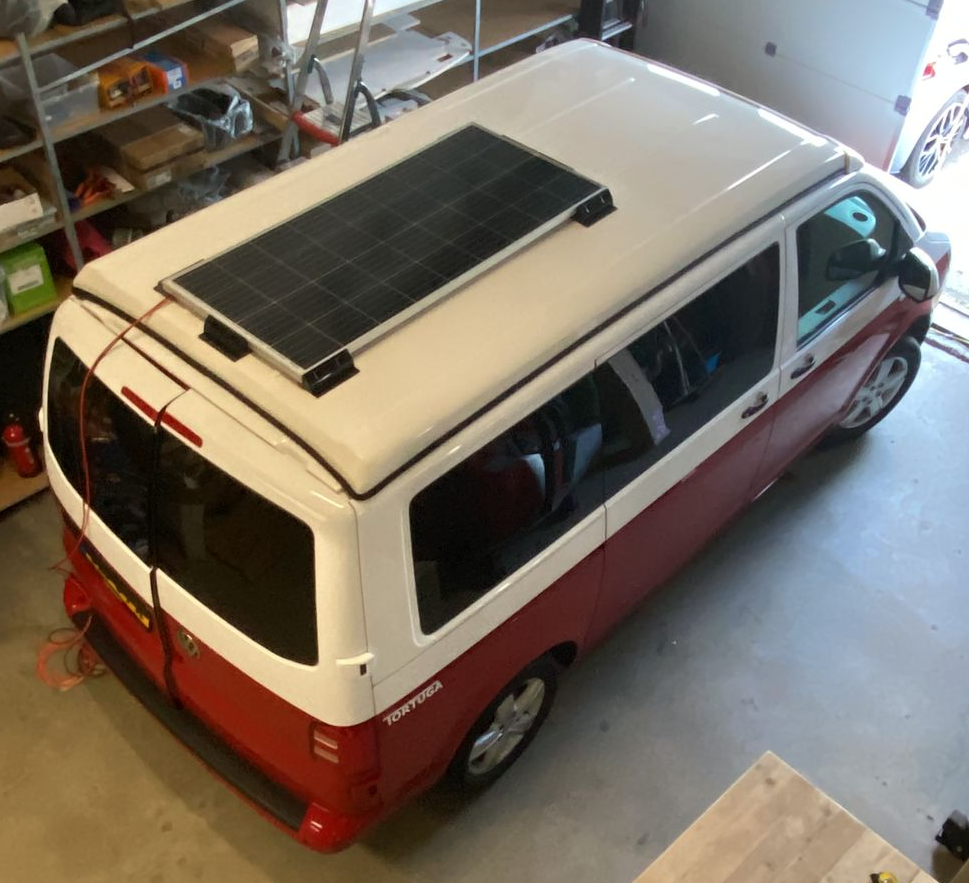Rood-witte bestelwagen met een zonnepaneel op het dak, geparkeerd in een garage.