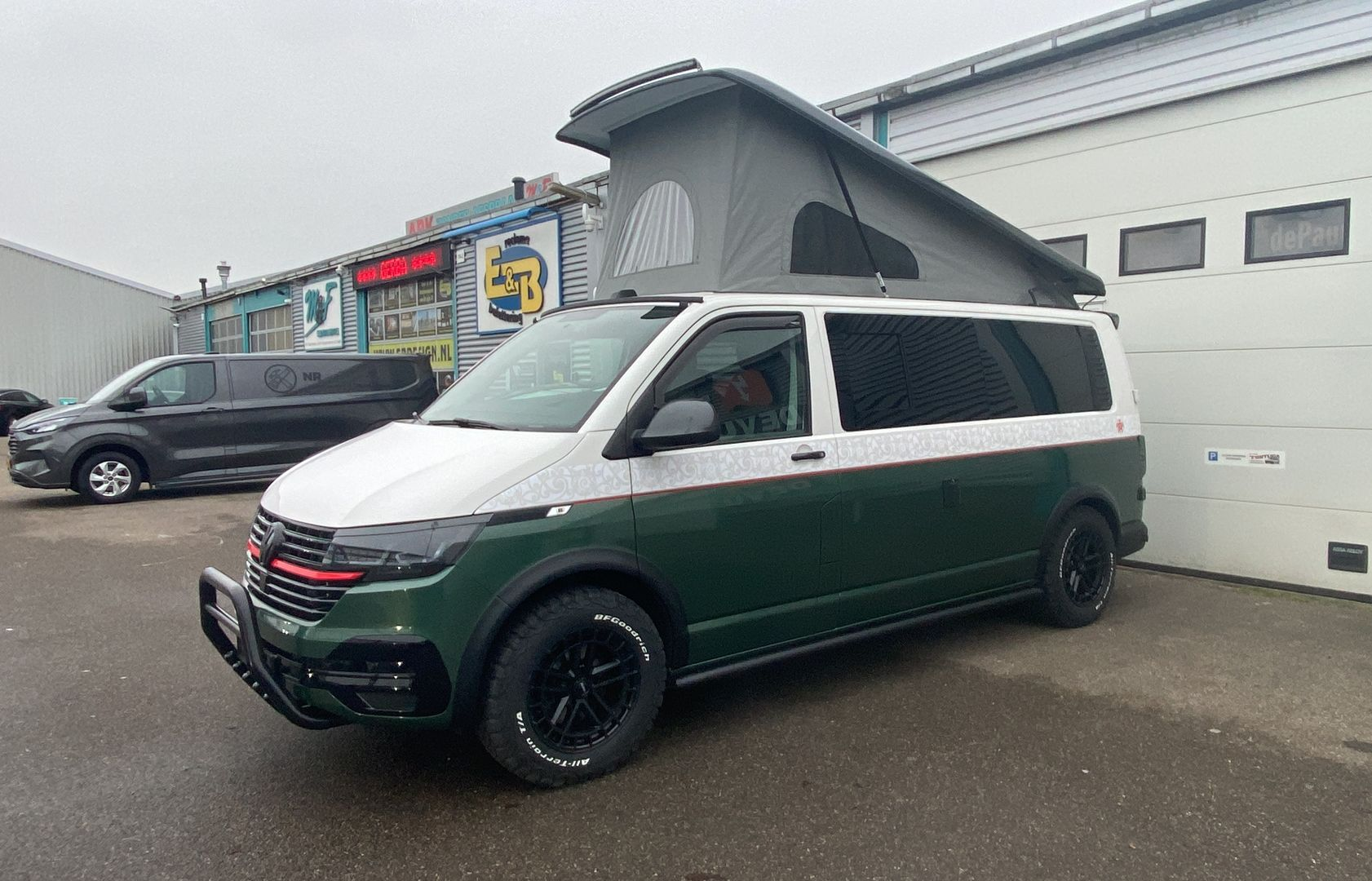 Groen-witte camper met hefdak geparkeerd voor een gebouw.