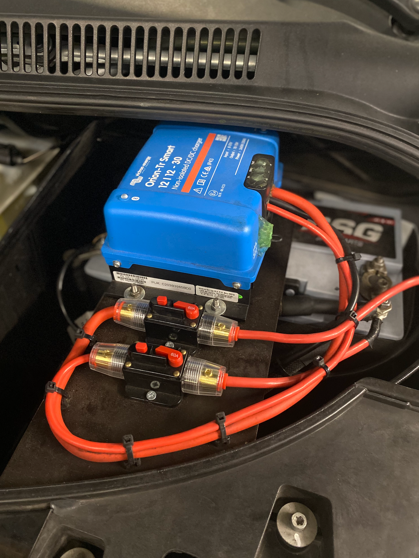 Blauwe Victron Orion-Tr DC-DC-lader, zwarte zekeringen, rode draden, in een autocompartiment.