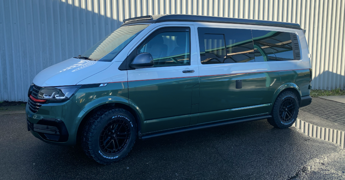 Een tweekleurige, groen-witte camper met zwarte wielen staat buiten geparkeerd.