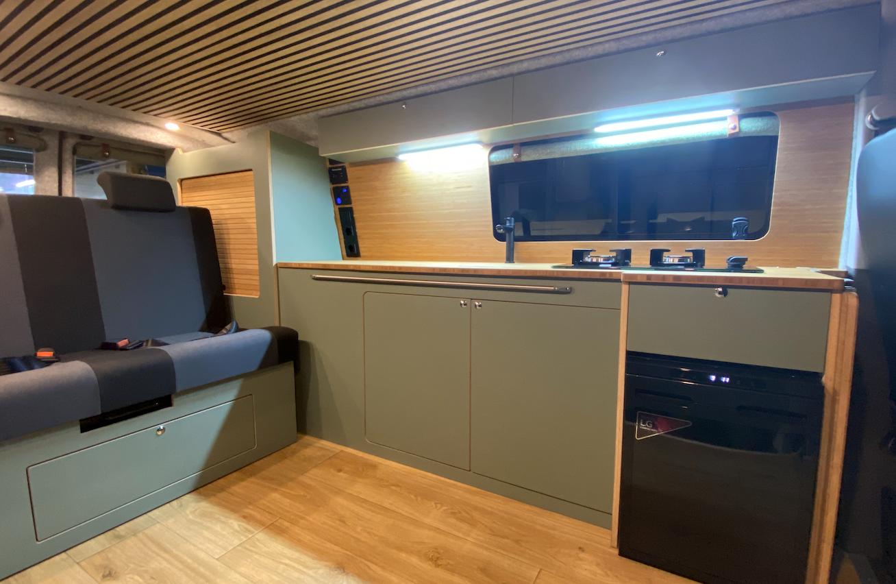 Interieur van een omgebouwde camper met groene kastjes, houten accenten en een zitje.