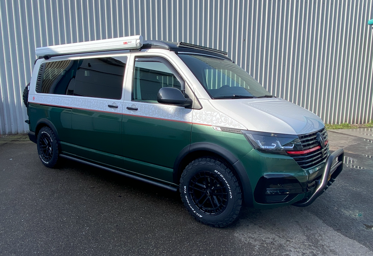Een camperbusje geparkeerd in een bos, met campingstoelen, een tafel en een rugzak buiten opgesteld.