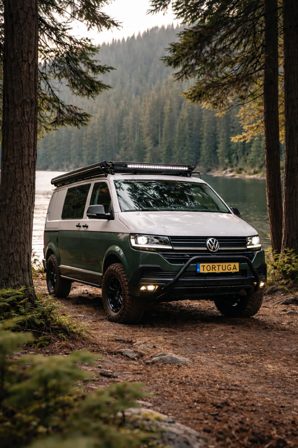 Groen-witte camper geparkeerd op een pad langs een meer; bomen op de achtergrond.