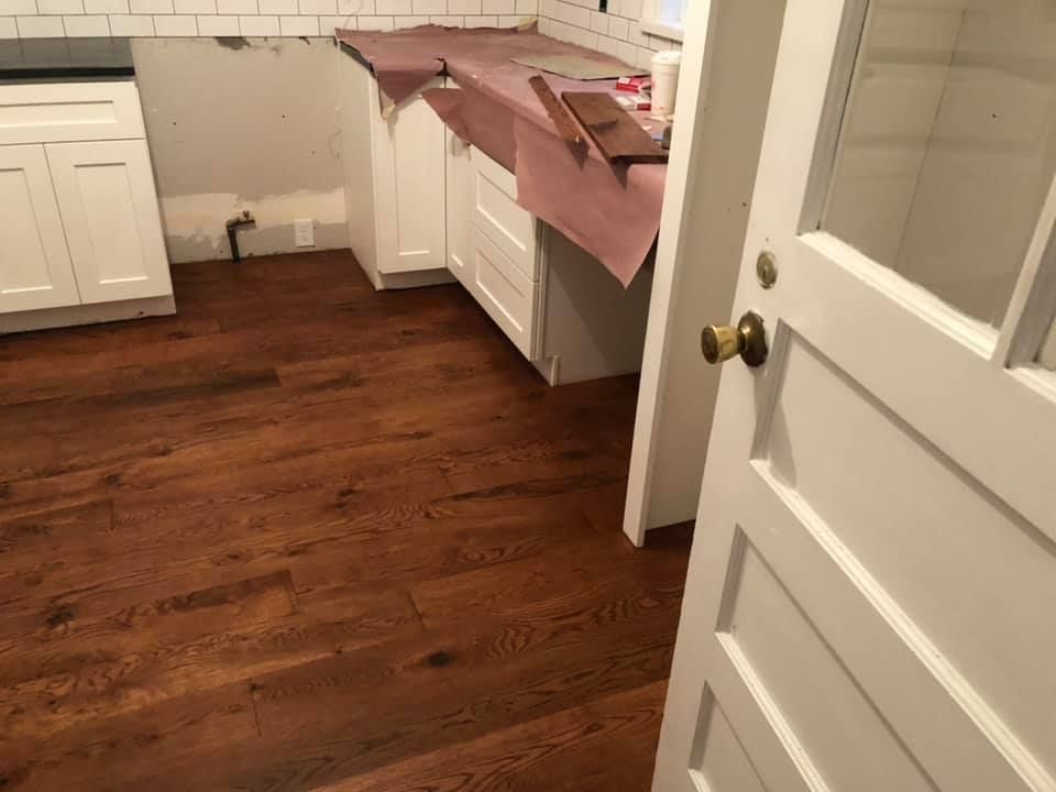 Hardwood flooring in a kitchen renovation; white cabinets and open door.