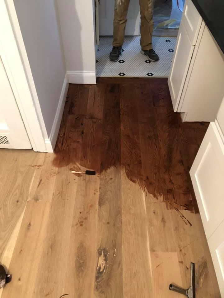 Wood floor being stained, half finished. A person stands in the doorway.