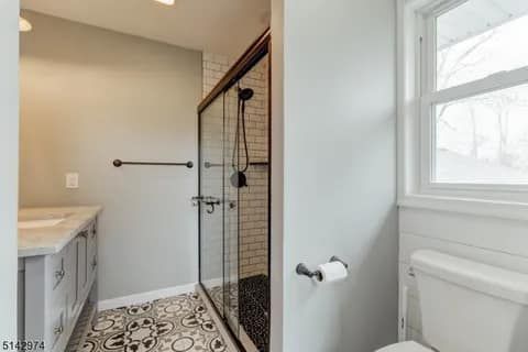 Bathroom with gray walls, white toilet, glass shower, and patterned floor tiles.