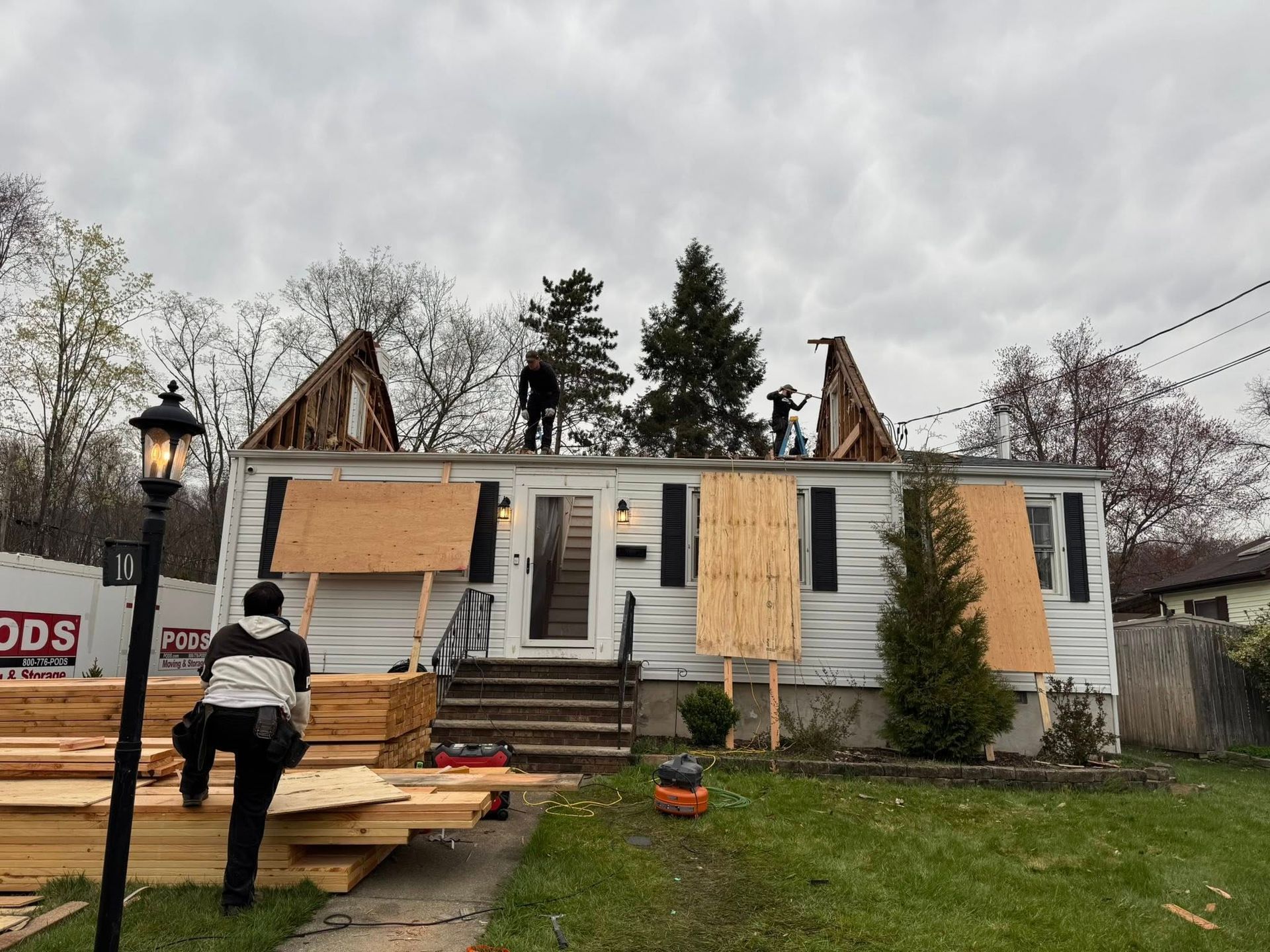 Workers rebuilding a house roof. Boards and tools are on the lawn. Overcast sky.