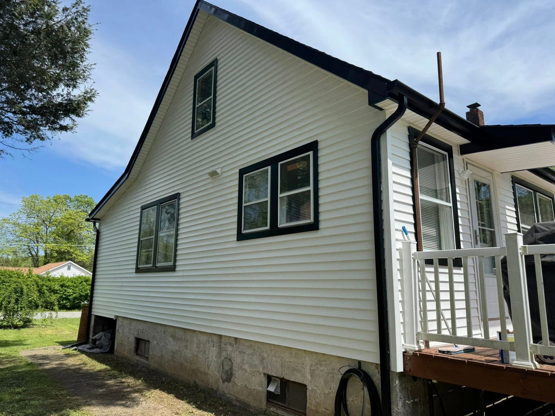 White house with black trim, windows, and gutters. A porch with a white railing is on the right.
