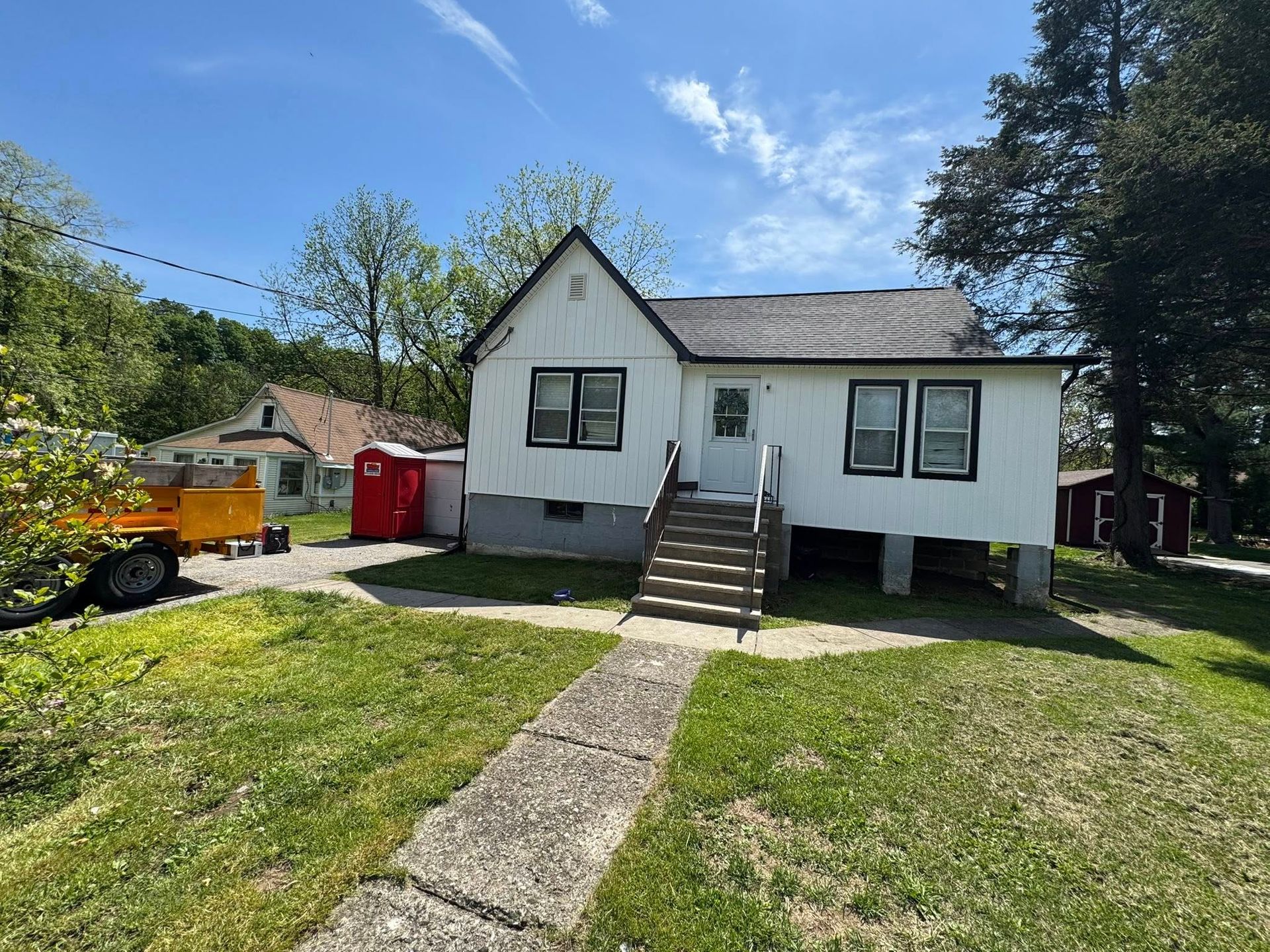 White house with dark trim and stairs, grassy yard, pathway to door, sunny day.
