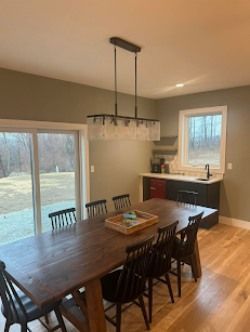 Dining room with a long wooden table, black chairs, and a bar area with a window.