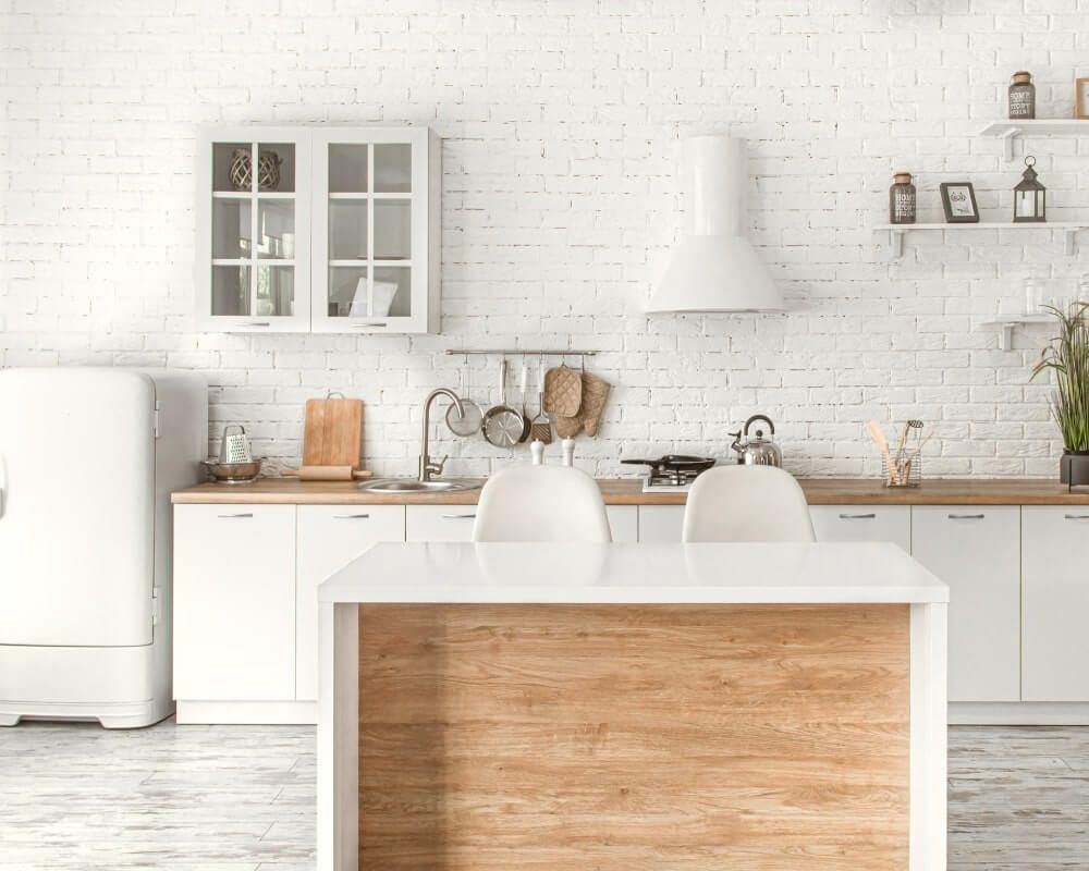 White kitchen with wood-tone island. Features refrigerator, cabinets, range hood, and shelves with decorative items.