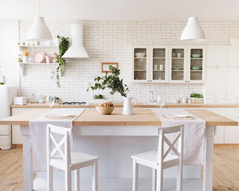 White kitchen with island, brick wall, wood cabinets, and pendant lights.