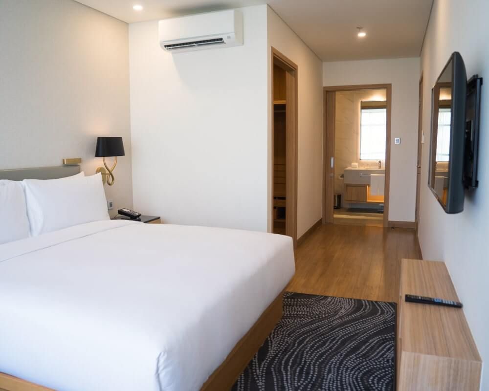 Hotel room with a bed, TV, and en-suite bathroom. White walls, wooden floor, and modern decor.