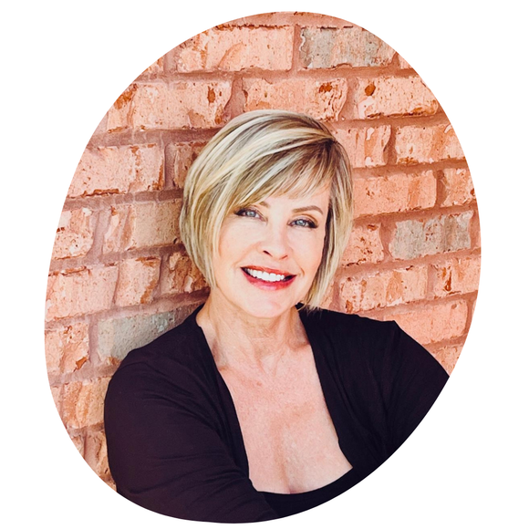 Woman with blonde bob smiles against a brick wall. She wears a black top.