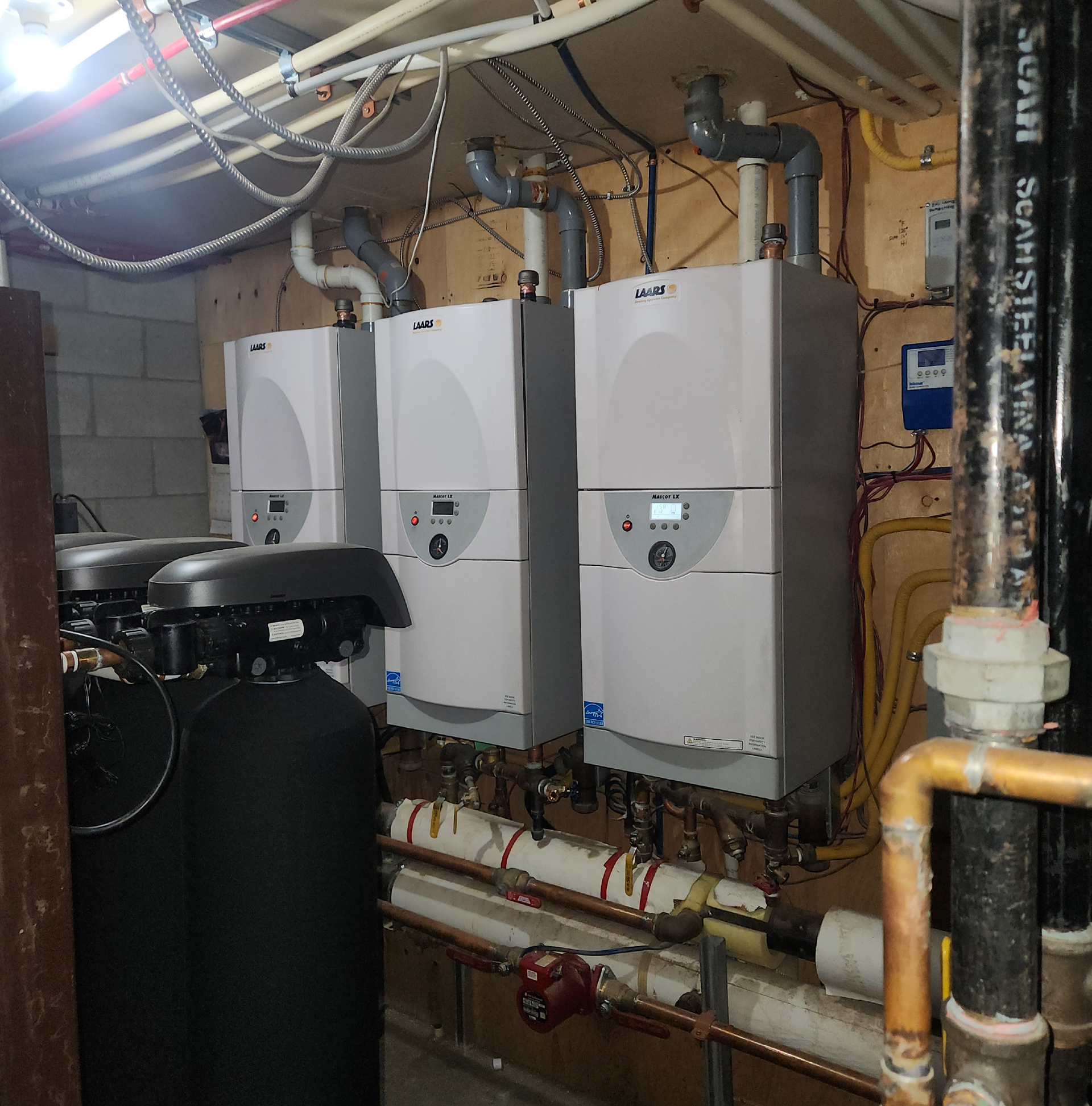 Une rangée de chaudières est alignée dans une pièce avec des tuyaux