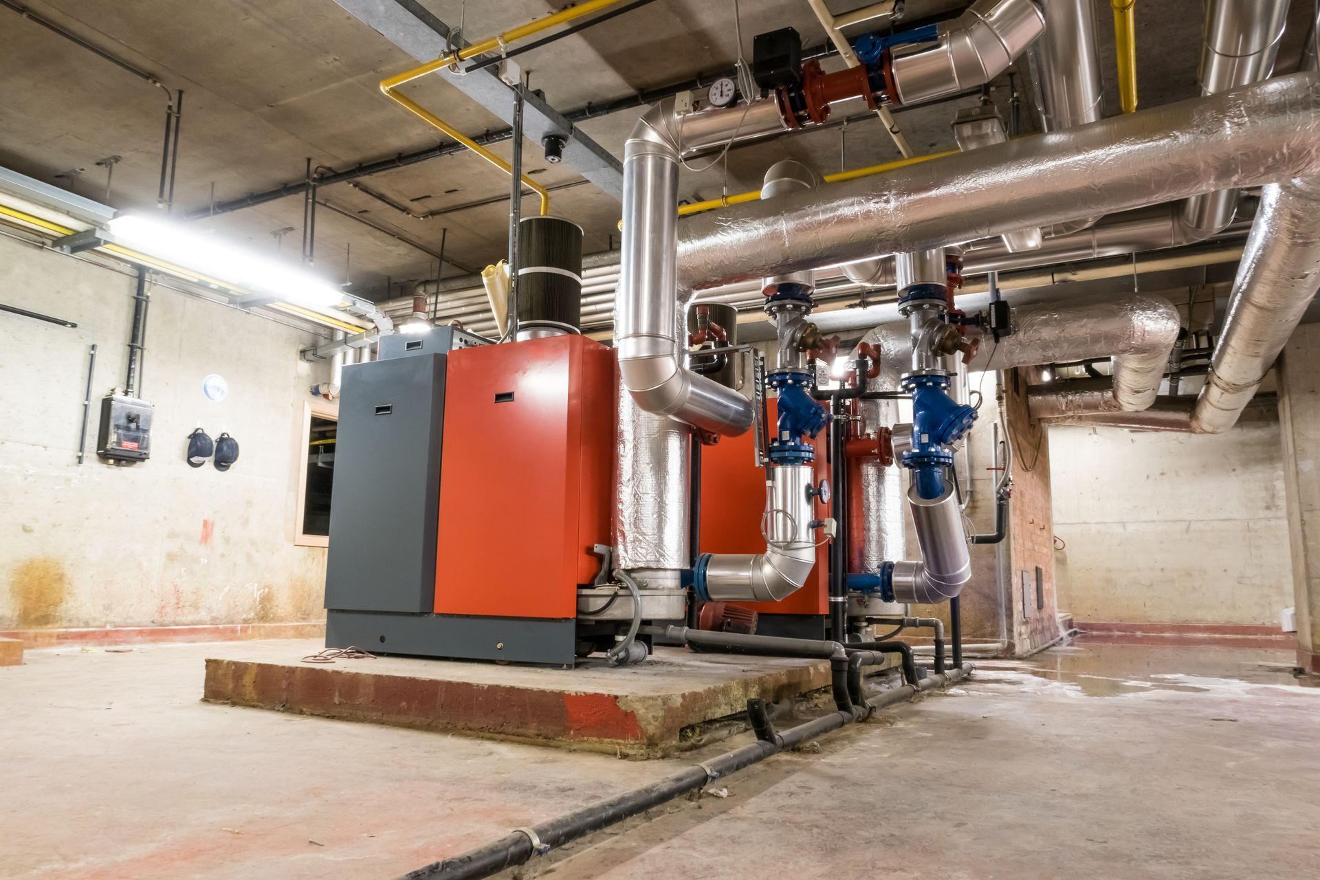Une pièce avec beaucoup de tuyaux et une chaudière dedans.