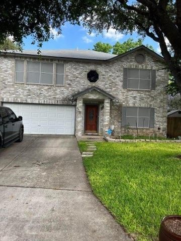 A two-story stone house with a double garage, a dark red front door, and a green front lawn under a blue, cloudy sky.
