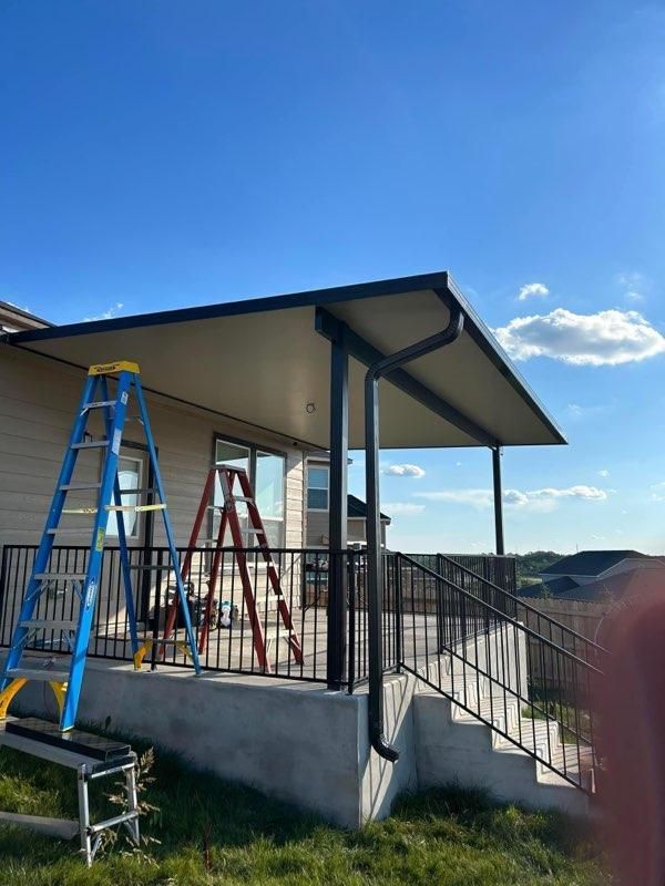 A newly constructed black-framed deck cover and railing attached to the back of a house with two ladders on the deck.