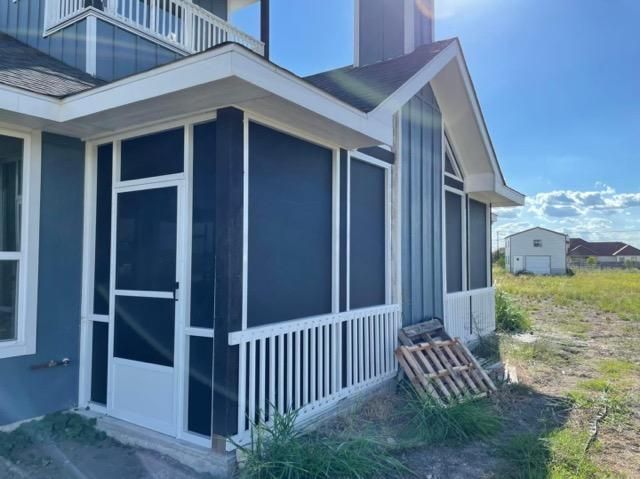 A blue-sided house featuring a white-framed screened porch with a door and white railings, viewed on a sunny day.