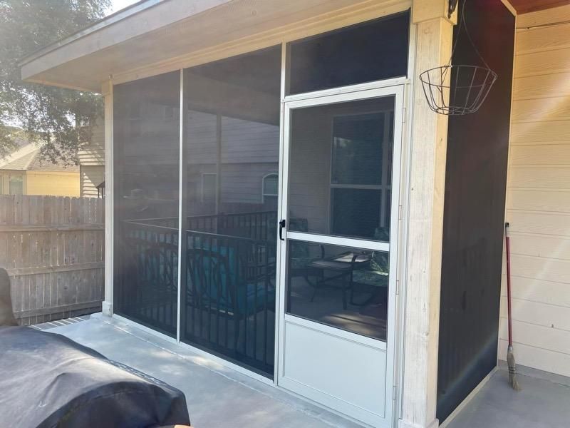 A screened-in patio porch with a white frame door and a view of outdoor furniture, situated next to a wooden fence.