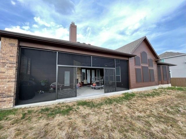 A brick-and-siding house with a large screened-in porch on the back, situated on a grassy lot under a cloudy blue sky.