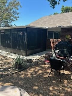 A backyard patio with a screened-in enclosure, gravel ground, and outdoor chairs on a sunny day.