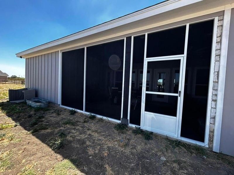 A white-framed screened porch with a glass storm door attached to the back of a house with light gray vertical siding.