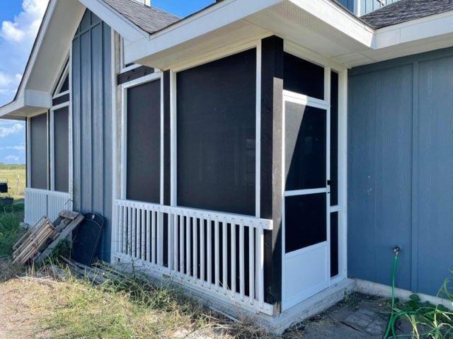 A screened-in porch with a white railing and frame, attached to a house with blue siding under a blue sky.