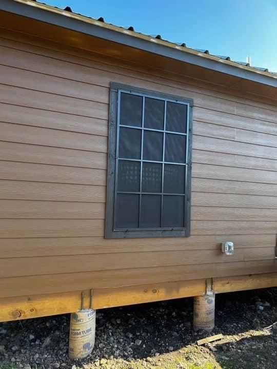 A brown house exterior with tan lap siding, a metal-framed window with screen, and a pier and beam foundation.