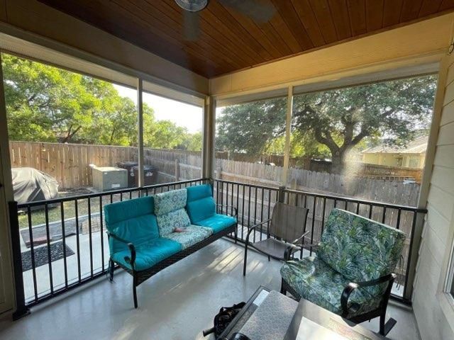 A screened-in porch with a teal sofa and a patterned armchair, featuring a wood-paneled ceiling and a view of a backyard.