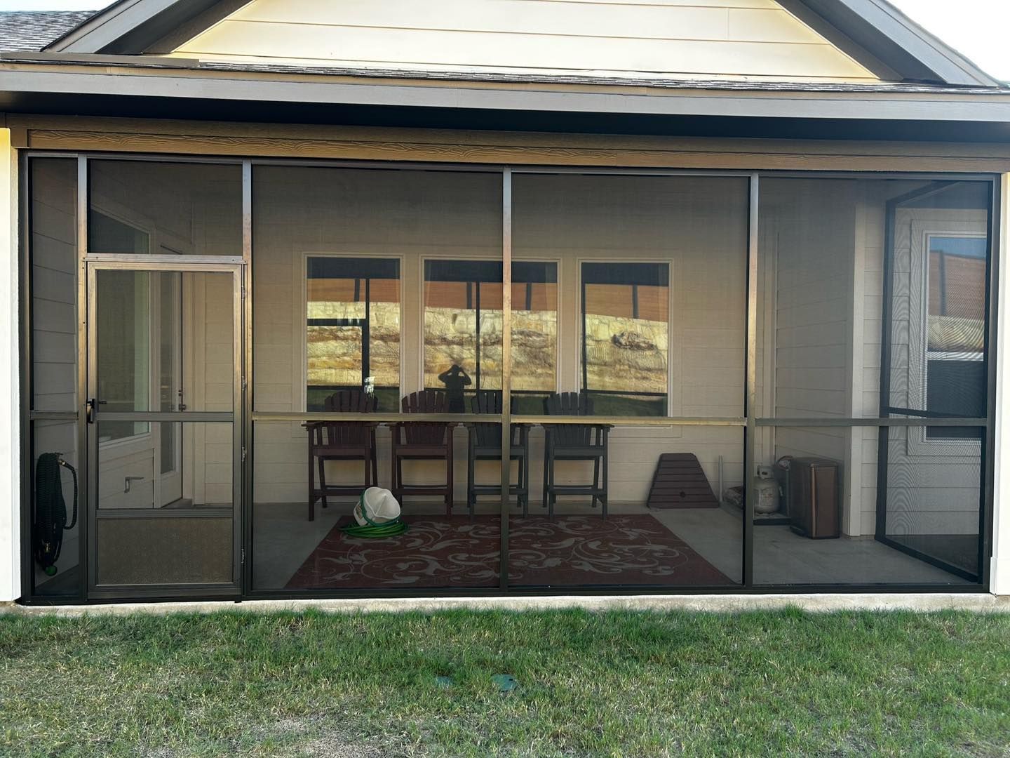 A screened-in patio with a dark metal frame, containing a table and chairs, visible through a patterned rug on the floor.