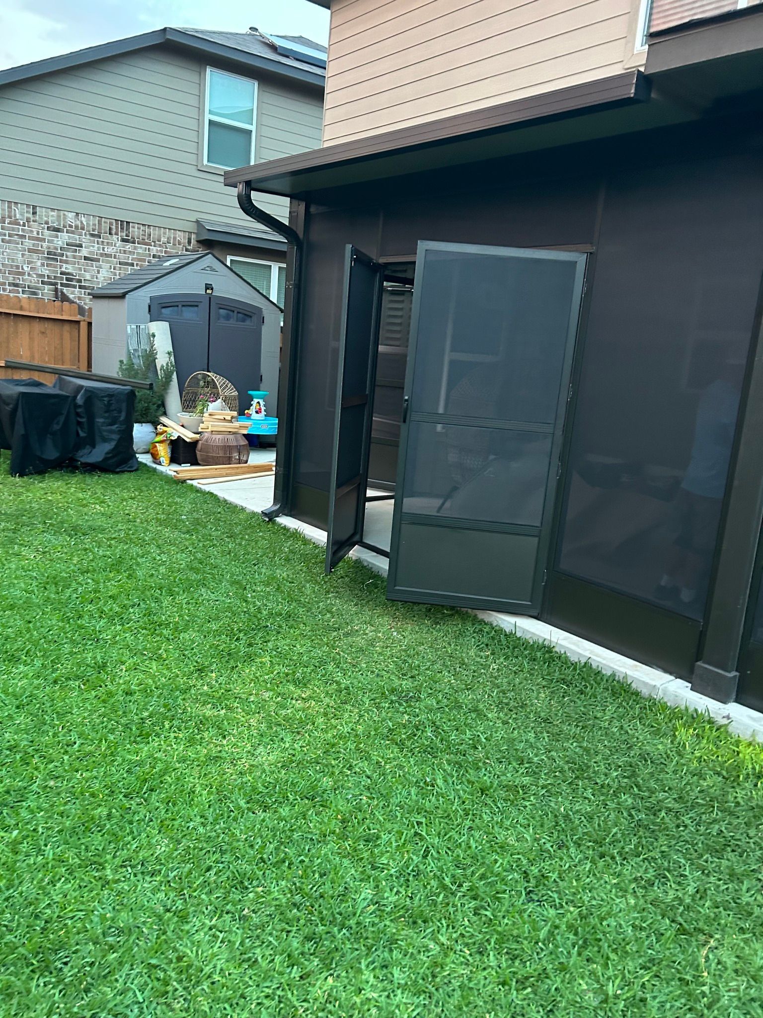 A view of a backyard grass lawn leading up to an enclosed patio with a dark screen door left partially open.