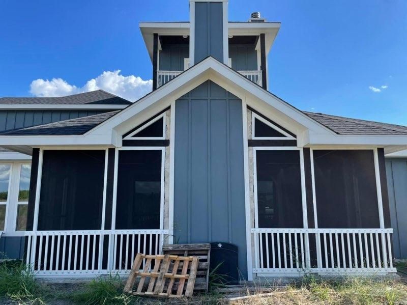 Blue house with a screened-in porch, white railings, and a central chimney tower against a clear blue sky.