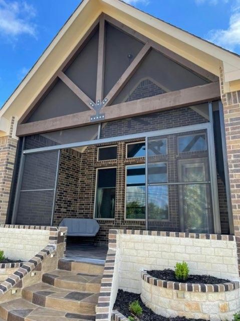 A screened-in porch with a gabled roof, brick exterior, and stone steps leading up to the entrance.